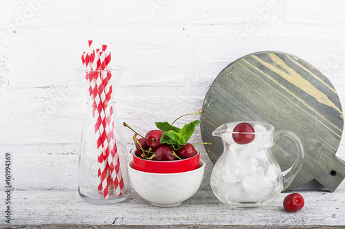 Kitchen still life white brick wall: kitchen utensils, cutting board, ice cubes for cocktails, berries, cocktail tubes for a holiday in the backyard. In the horizontal photo