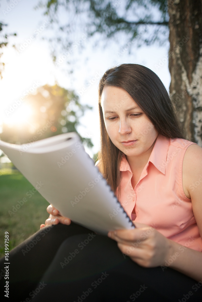 Pretty young brunette girl studying in the park and preparing for an exam, looking concentrated Pretty young brunette girl studying in the park and preparing for an exam, looking concentrated