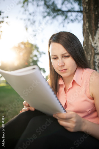 Pretty young brunette girl studying in the park and preparing for an exam, looking concentrated