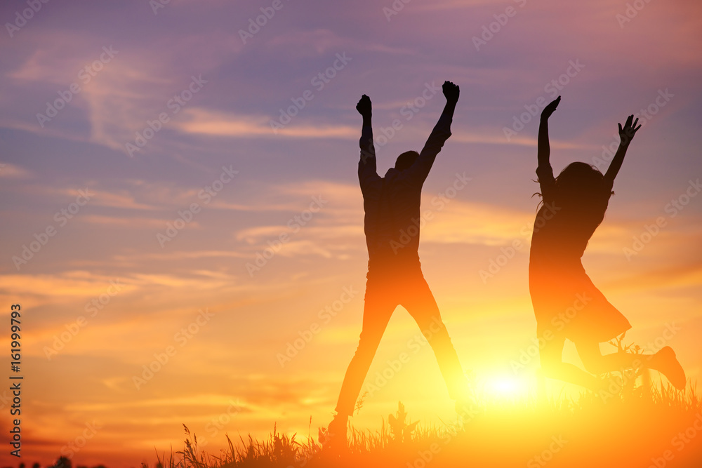A young man with his girlfriend jump on background sunset silhouette