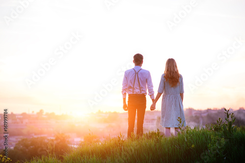 young couple is holding hands on a background sunset