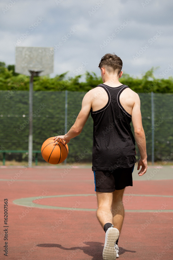 Teenage boy bouncing a basketball on a court