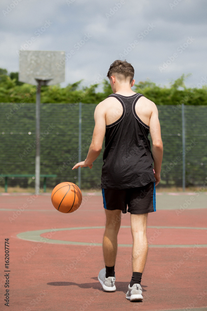 Teenage boy bouncing a basketball on a court