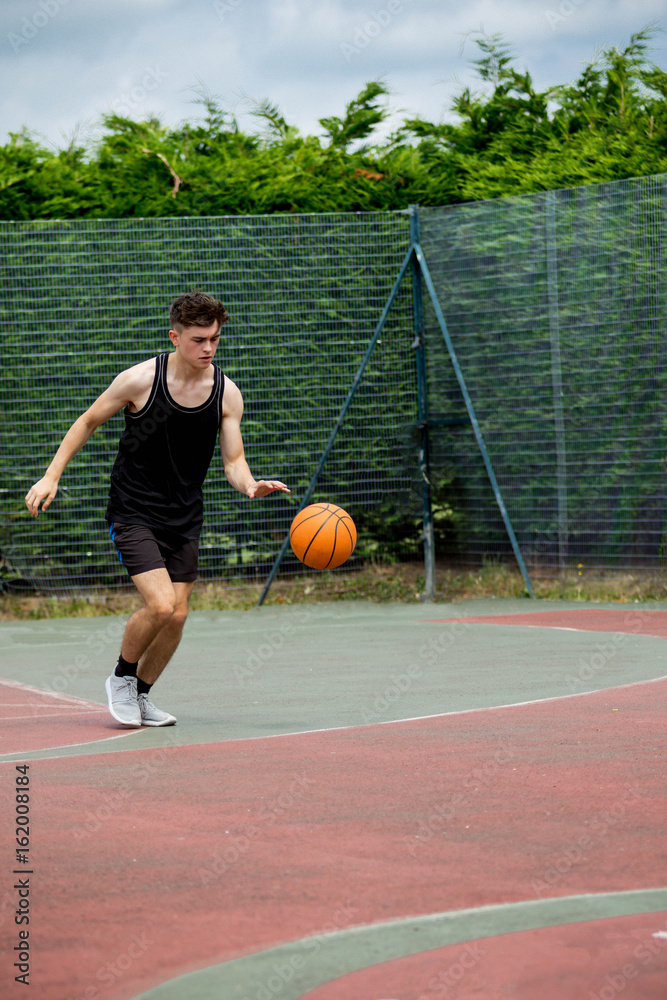 Fototapeta premium Teenage boy bouncing a basketball on a court