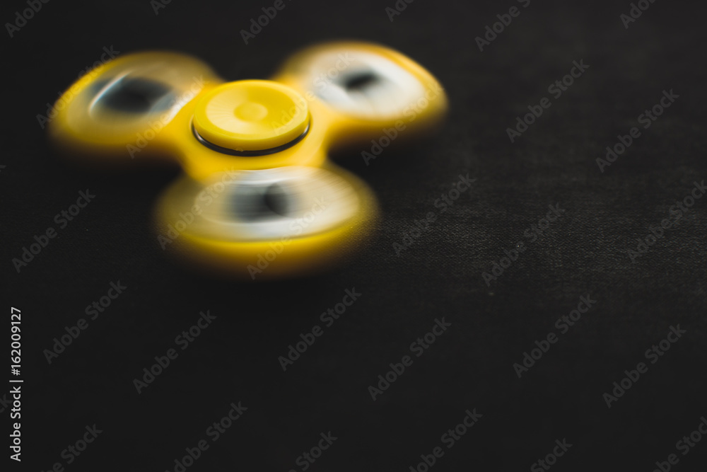 Rotating yellow fidget spinner device on black background. Top view. Playing with a yellow hand spinner fidget toy Rotating yellow fidget spinner device on black background. Top view. Playing with a yellow hand spinner fidget toy