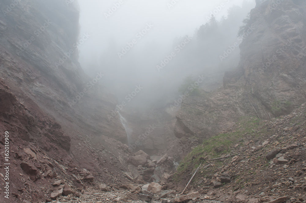 Waterfall in red sandstones covered by fog in Bletterbach canyon, Dolomites, Italy