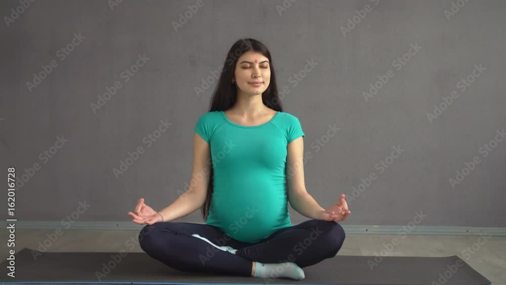 Pregnant ethnic girl engaged in yoga sitting in a lotus pose. Indian woman with hindi Pregnant ethnic girl engaged in yoga sitting in a lotus pose. Indian woman with hindi