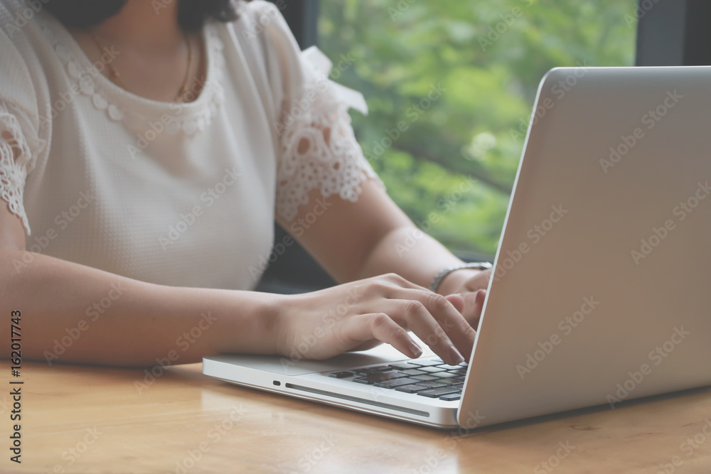 Fototapeta premium Concentrated at work. Confident young woman in smart casual wear working on laptop while sitting near window in creative office or cafe