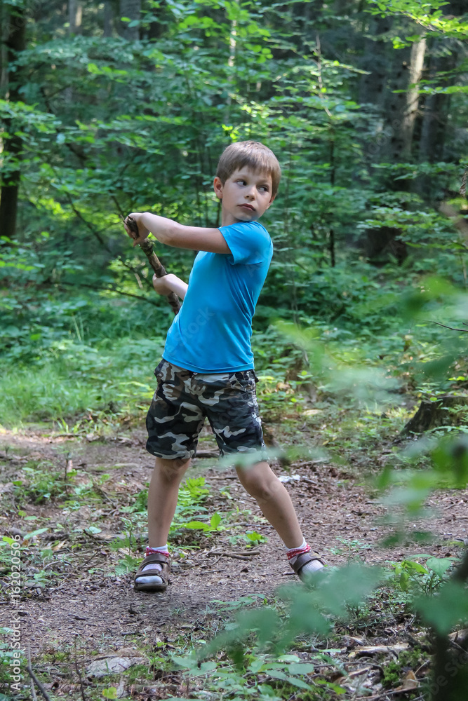 Boy with wooden stick in summer forest park