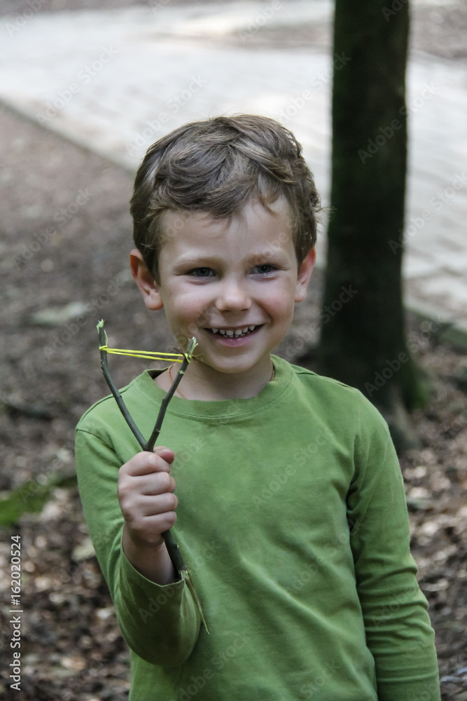 Smiling boy with makeshift slingshot in summer forest park Smiling boy with makeshift slingshot in summer forest park