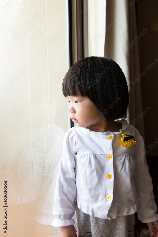 Asian toddler watching the rain through window Asian toddler watching the rain through window