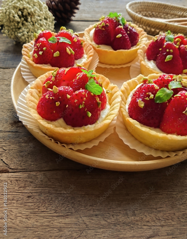 Homemade strawberry tart in paper cup on wood plate. Fruit tart or strawberry tart sprinkle with chopped pistachio and decorated with mint leaf. Delicious strawberry tart on rustic wood background. Homemade strawberry tart in paper cup on wood plate. Fruit tart or strawberry tart sprinkle with chopped pistachio and decorated with mint leaf. Delicious strawberry tart on rustic wood background.