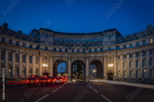 Admiralty Arch at night with light trails from passing cars there is a red trail on the left side and a white one on the right side near Trafalgar Square in London as the entrance to The Mall