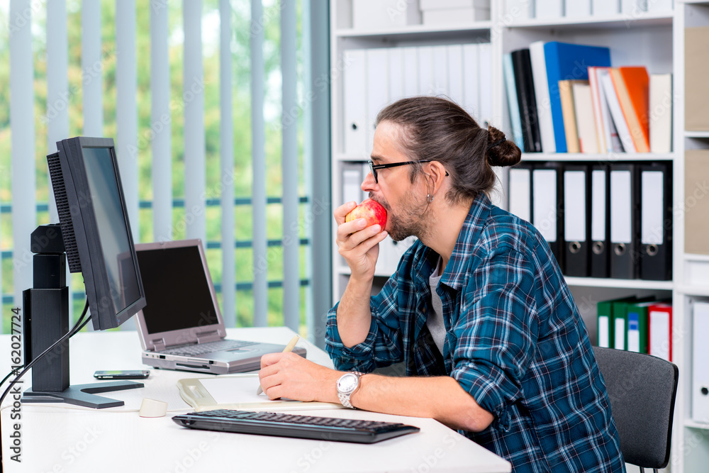 Fototapeta premium man is working in his officeand eating apple