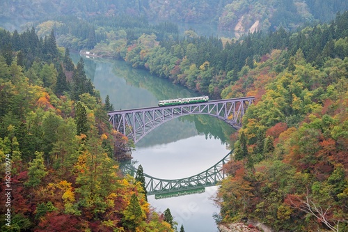 First bridge and Tadami river in beautiful autumn season with train crossing the bridge.