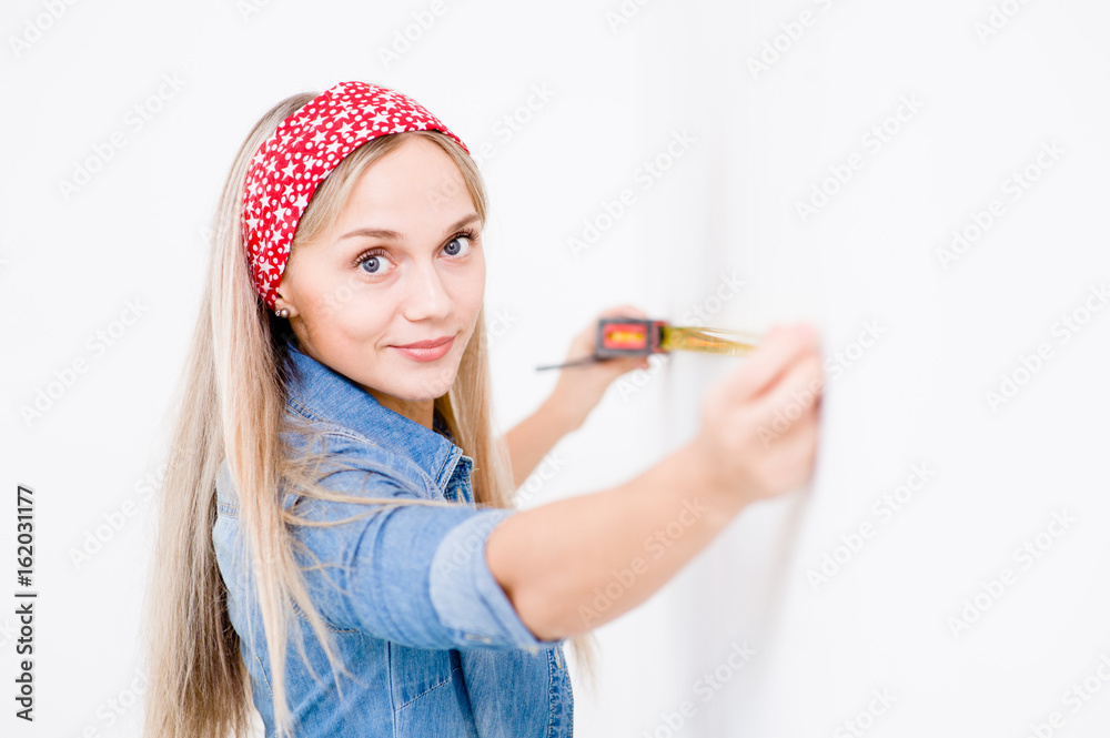 Beautiful young woman measuring a wall with measuring tape Beautiful young woman measuring a wall with measuring tape
