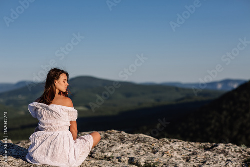 Beautiful girl remains on top of a mountain and looks at the horizon with a beautiful background. A colorful photo of a natural sunset, a miracle, incredible, a dance, hair in the wind