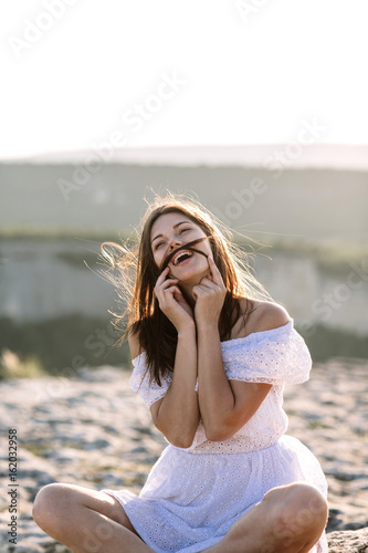 Beautiful girl remains on top of a mountain and looks at the horizon with a beautiful background. A colorful photo of a natural sunset, a miracle, incredible, a dance, hair in the wind © boykovi1991