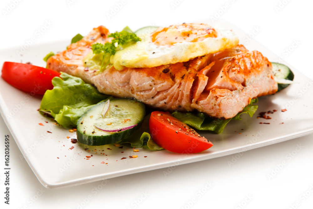 Grilled salmon with fried egg and vegetables on white background Grilled salmon with fried egg and vegetables on white background