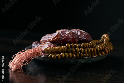 Close-up of Dates for iftar and prayer rosary beads on black wooden table. Islamic religion and ramadan month concept.