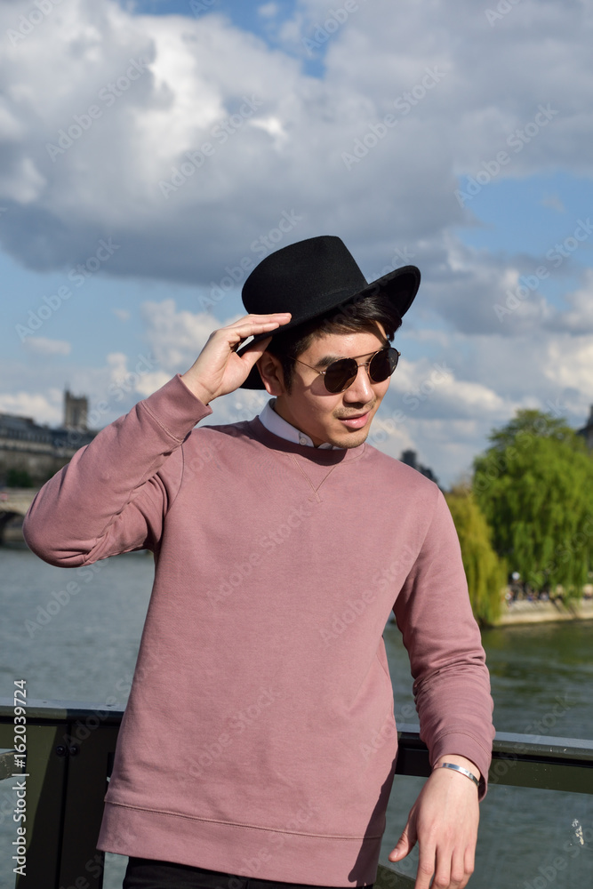 Paris,France -April 2,2017:  Young Good looking Asian man in pink shirt and black hat on Pont des Arts bridge  in Paris.
