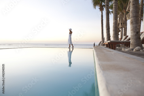 femme au bord d'une piscine à la mer au coucher du soleil