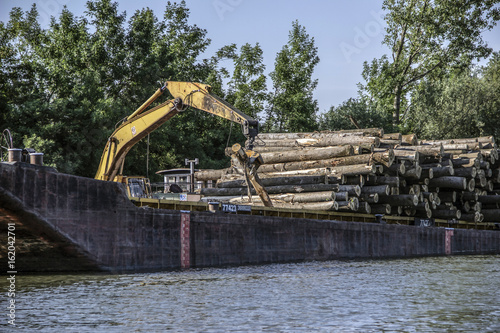 Crane with jaws loading logs onto a river barge