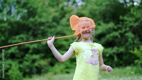On the green, chamomile lawn, child , girl plays with net, fools around. She has fun. Summer, outdoors, in the forest. Vacation with children photo