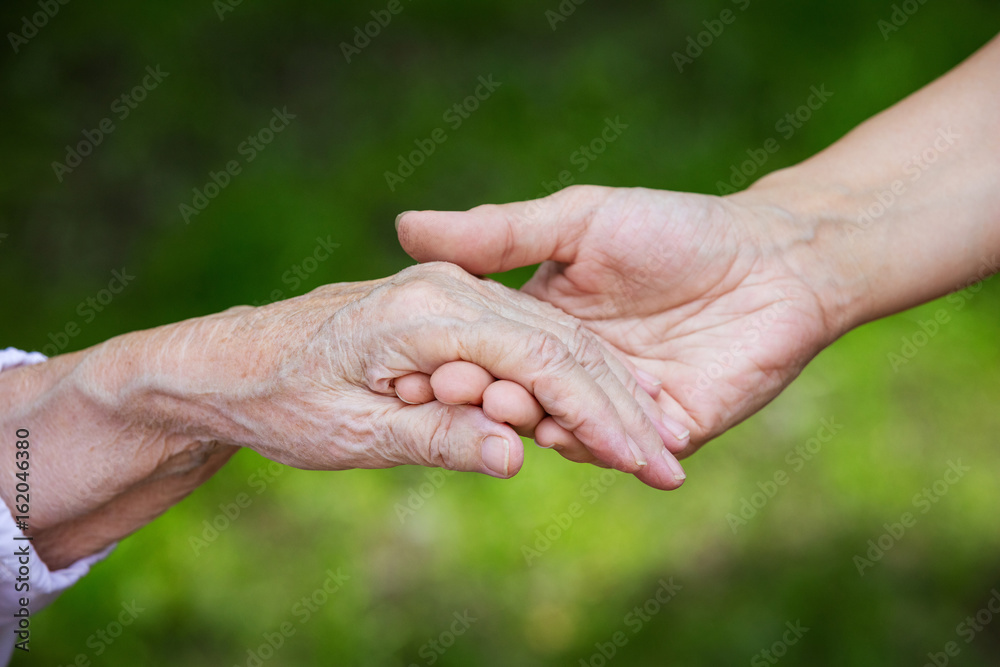 Hands of young adult and senior women over green background Hands of young adult and senior women over green background
