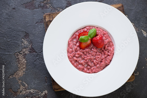 Above view of a white plate with strawberry risotto on a brown stone background, horizontal shot