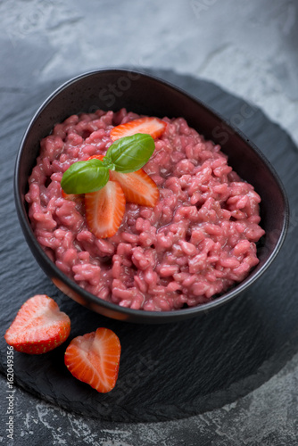 Risotto with strawberries served in a black bowl on a stone slate tray, selective focus, studio shot