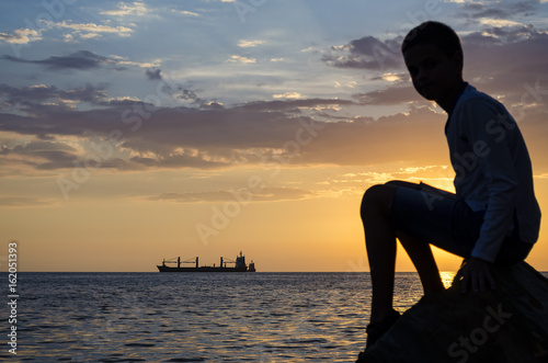 Silhouette of the ship over the sunrise and silhouette of the teenager photo