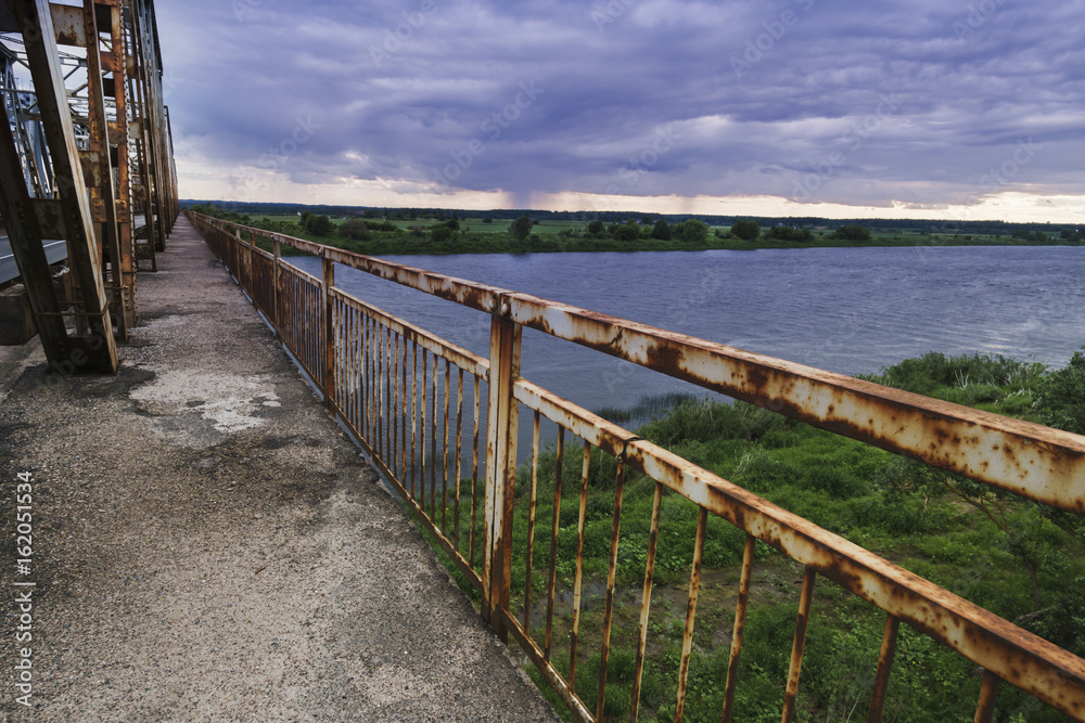 Fototapeta premium View of the old bridge at the dark rainy day over a river.