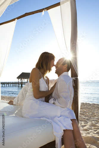 couple amoiureux au bord de la mer sur un lit blanc avec des voilages © plprod