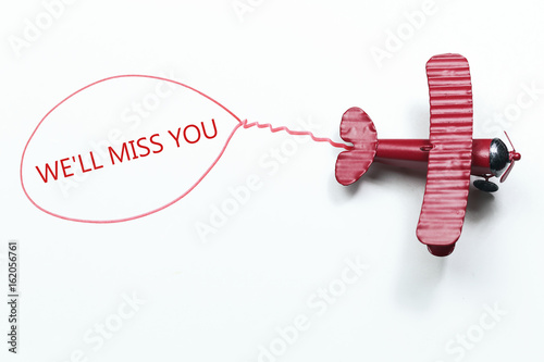 Konstfotografi writing We'll Miss You red toy airplane with talk bubble on white background