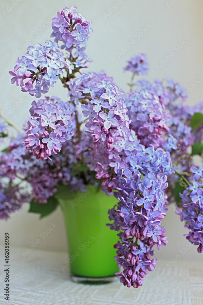 Lilac bouquet in green vase on light background