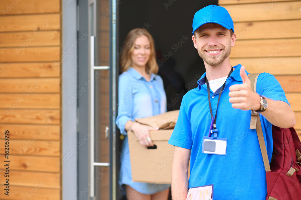 Smiling delivery man in blue uniform delivering parcel box to recipient - courier service concept Smiling delivery man in blue uniform delivering parcel box to recipient - courier service concept