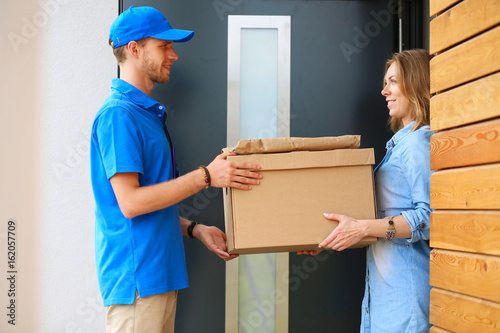 Smiling delivery man in blue uniform delivering parcel box to recipient - courier service concept photo