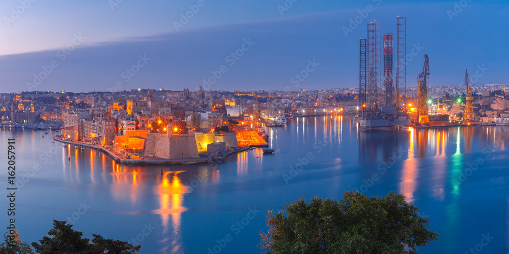Panoramic aerial skyline view of ancient defences of Three cities, three fortified cities of Birgu, Senglea and Cospicua and Grand Harbor with ships, as seen from Valletta during morning blue hour