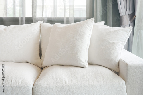 White color sofa and pillows with sheer curtain in background