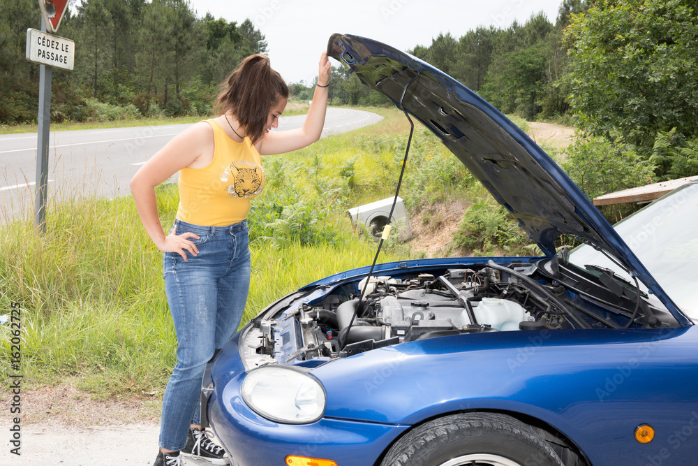 Beautiful woman standing in front of the bonnet of a broken down car in the countryside