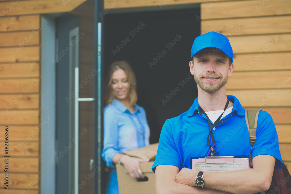 Smiling delivery man in blue uniform delivering parcel box to recipient - courier service concept Smiling delivery man in blue uniform delivering parcel box to recipient - courier service concept