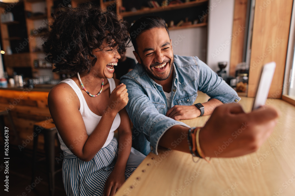 Obraz premium Laughing couple taking selfie at coffee shop
