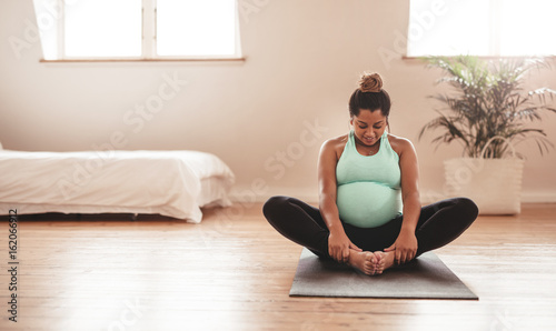 Beautiful expectant mother doing yoga at home