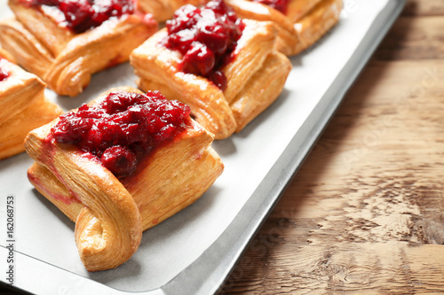 Tray with delicious puff pastries and cherry on wooden table