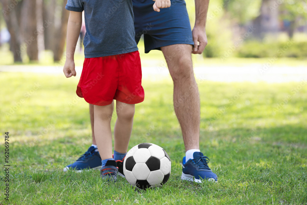 Father and son playing football on green grass in park Father and son playing football on green grass in park