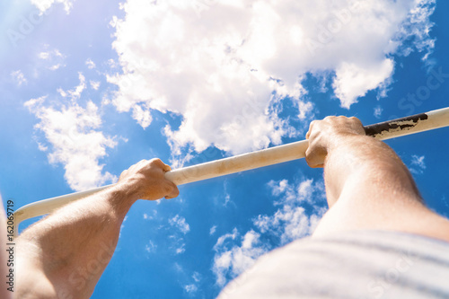First-person view of the horizontal bar. The guy pulls up on the bar. Workout outdoors. Blue sky on blackground