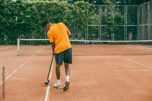 A young man in a sports uniform is cleaning a tennis court. The tennis player is preparing a court for the game. © belyjmishka