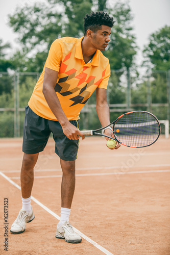 Young tennis player with racket ready to serve a tennis ball. Professional tennis player starting set. © belyjmishka