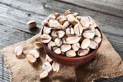 Canvas Print Pistachios in wooden bowl over wooden background, selective focus